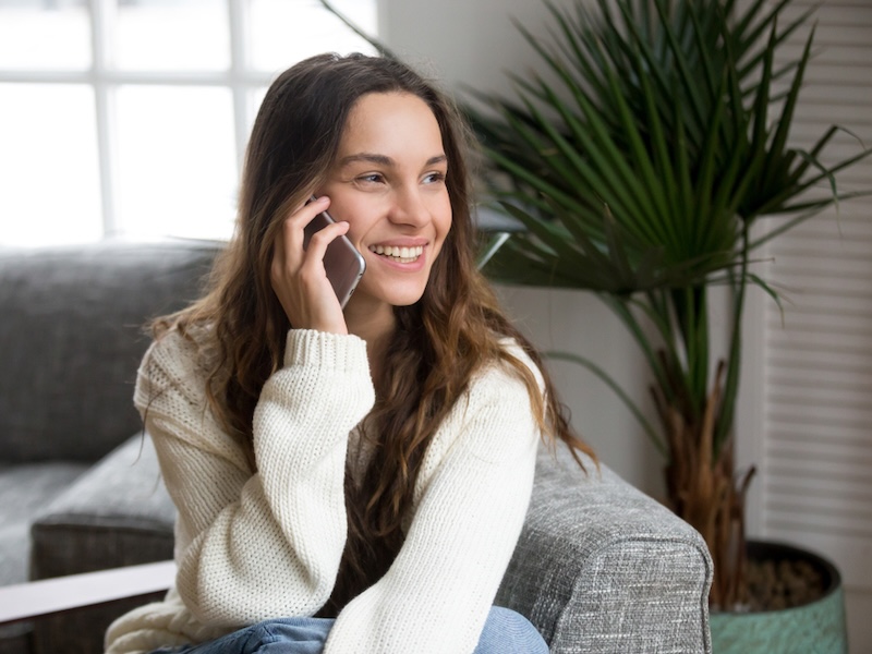 Young woman speaking with friend on phone at home